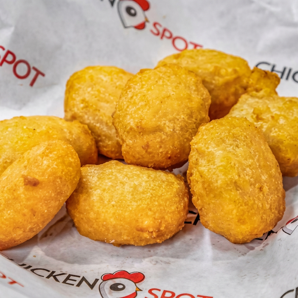 Golden fried chicken nuggets arranged on branded Chicken Spot paper in a red serving tray.